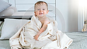 Smiling baby in white towel after having bath sitting on bed