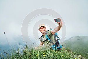 Smiling backpacker man taking selfie picture using smartphone and showing Thumbs Up during walking by the foggy cloudy weather