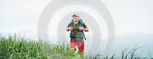 Smiling backpacker walking by the foggy cloudy weather mountain range path with backpack. Active sport backpacking healthy