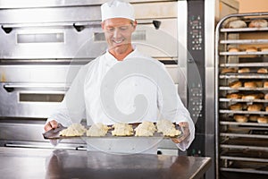 Smiling baker holding tray of raw dough