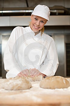 Smiling baker kneading dough in bakery