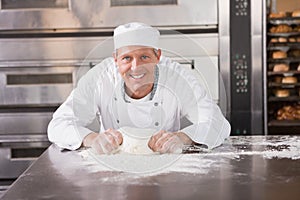 Smiling baker kneading dough on counter