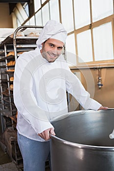 Smiling baker leaning on industrial mixer