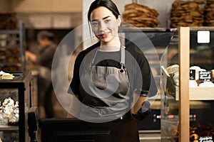 Smiling baker woman standing with fresh bread and pastry at bakery. Young woman in her bake shop and looking at camera