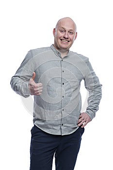 Smiling bald man. A guy in a gray shirt and blue trousers stands and shows like with his hands. Positive and optimistic. Isolated