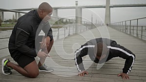 Smiling bald man motivating his friend who doing push ups
