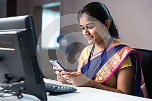smiling bank employee busy using mobile phone at office infront of computer - concept of relaxation, customer service