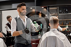 Smiling barber sprinkling water on client`s haircut using sprayer bottle.