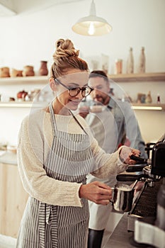 Smiling barista frothing fresh milk for cappuccino.