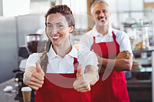 Smiling barista gesturing thumbs up with colleague behind