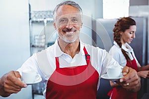 Smiling barista holding cups of coffee with colleague behind