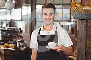 Smiling barista offering cup of coffee to camera