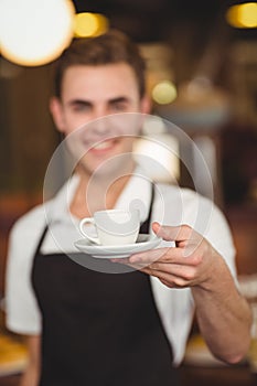 Smiling barista offering cup of coffee to camera