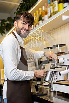 Smiling barista standing near coffee machine and looking contented