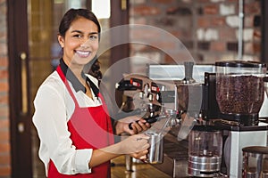 Smiling barista steaming milk at the coffee machine