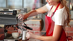 Smiling barista steaming milk at the coffee machine