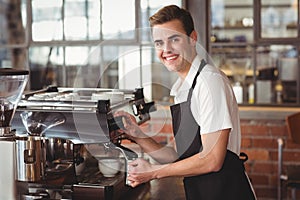 Smiling barista steaming milk at coffee machine