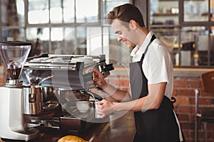 Smiling barista steaming milk at coffee machine