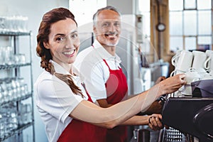 Smiling barista using the coffee machine with colleague behind