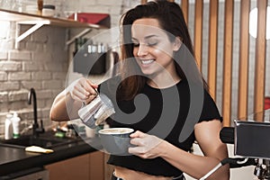 Smiling barista woman showing the process of pouring whipped cream to hot coffee drink barista work