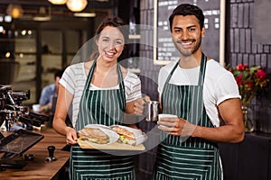 Smiling baristas holding sandwiches and hot milk