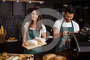 Smiling baristas holding sandwiches and making coffee