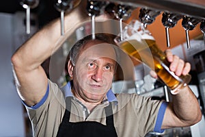 Smiling barman is pouring unbottled beer for next client