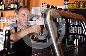 Smiling barman is pouring unbottled beer for next client