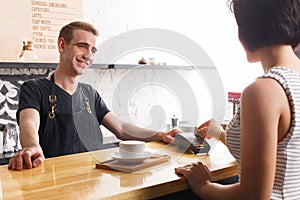 Smiling barman taking payment from client at counter of a coffee shop