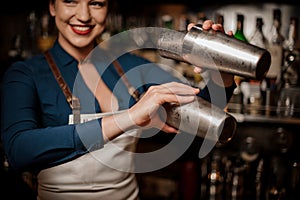 Smiling bartender girl holding two steel cocktail shakers