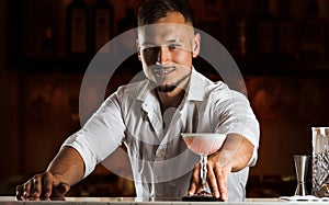 Smiling bartender gives the guest a chic cocktail in a tall glass.