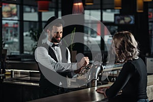 smiling bartender pouring beer from beer taps into glass and looking photo