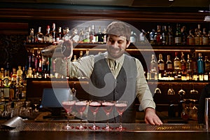 Smiling bartender pouring freshly prepared cocktail into several glasses
