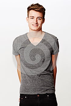 Smiling bashfully. Studio shot of young man smiling while standing with hands behind his back.