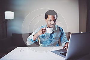 Smiling bearded African man making video conversation via laptop with partners while holding white cup black tea in