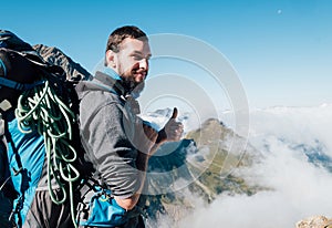 Smiling bearded climber with huge backpack with climbing rope showing thumb sign enjoying a French Apls valley with picturesque