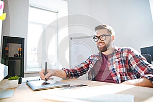 Smiling bearded designer drawing and using graphic pen tablet