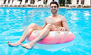 Smiling bearded guy enjoying the rest in the swimming pool while using inflatable ring. Man in sunglasses. Summertime