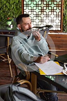 Smiling bearded man in casual clothes in cafe records audio messages