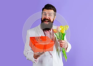 Smiling bearded man with gift box and bouquet of flowers. Businessman in suit with gift and bouquet of tulips. Romantic