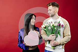 Smiling bearded man giving bouquet of flowers and gift box for beautiful woman. Portrait of happy romantic couple celebration