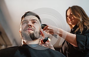 Smiling bearded Man portrait while undercut hairstyle hairdressing in Hair Salon by young hairdresser female. Modern barber shop