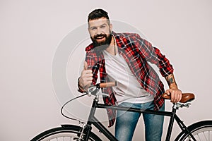 Smiling bearded man posing with bike and showing thumb up isolated photo