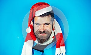 Smiling bearded man in santa hat and striped scarf looking through paper hole. Christmas sales.