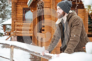 Smiling bearded man standing near wooden cottage in winter