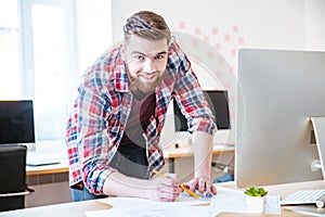 Smiling bearded man standing and working on blueprint in office