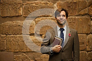 Smiling bearded schoolteacher in museum carrying books