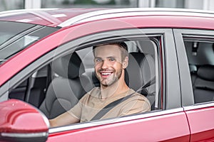 Smiling bearded young male driving red car