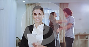 Smiling beautiful agent house woman looking straight to the camera while on the background couple are hugging happy each