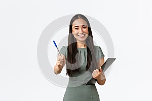 Smiling beautiful asian female shop assistant, employee asking to sign blank or shipping form, giving you pen as holding